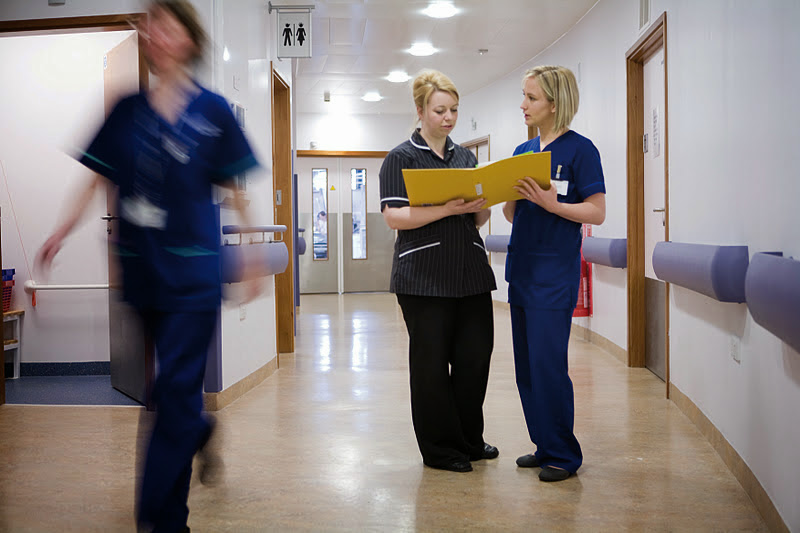 Nurse and advanced clinical practitioner talking in the hallway of a hospital